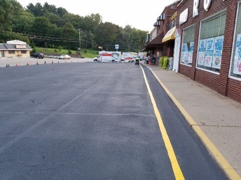 Empty parking lot beside a brick building with yellow curb lines and trees in the background