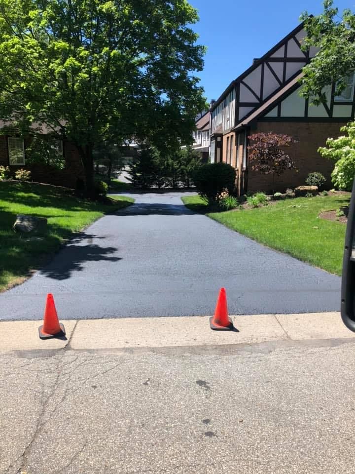 Freshly paved driveway entrance with two orange cones beside brick buildings and trees