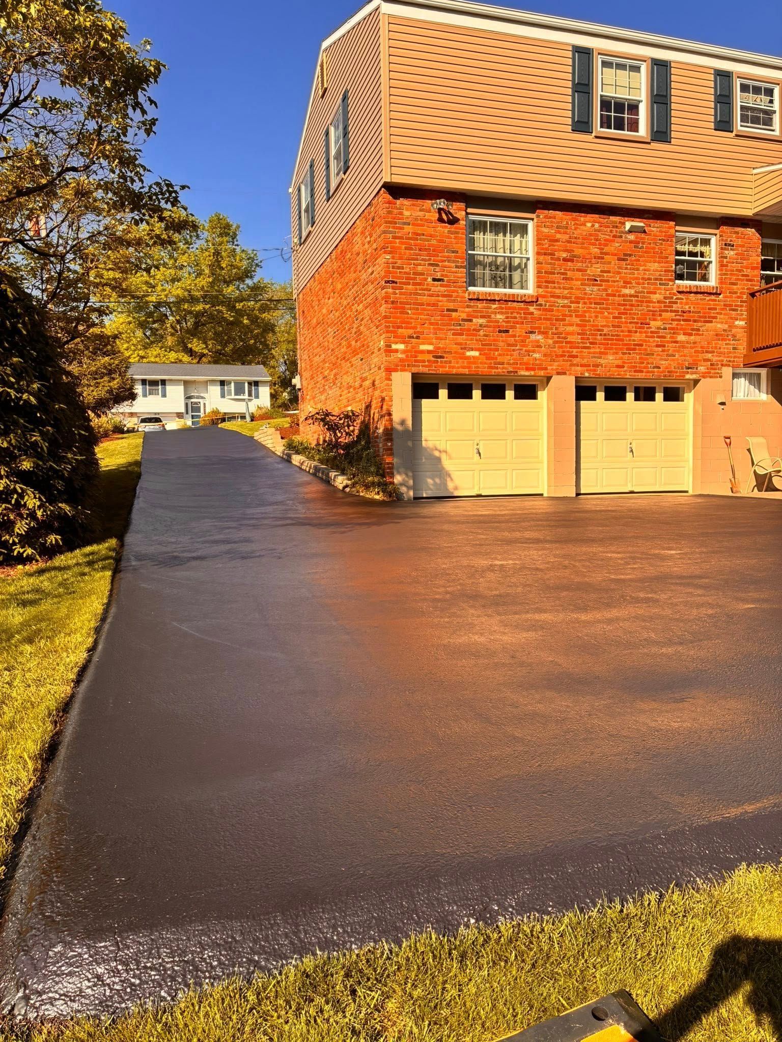 Brick house with tan garage doors and a long wet asphalt driveway in autumn sunlight