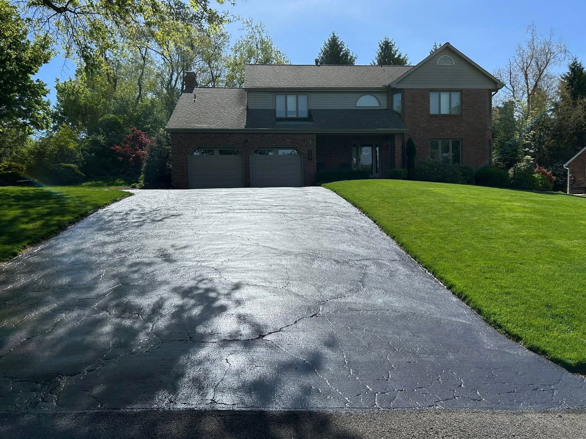 Suburban brick house with a steep black driveway and green lawn under bright sunlight