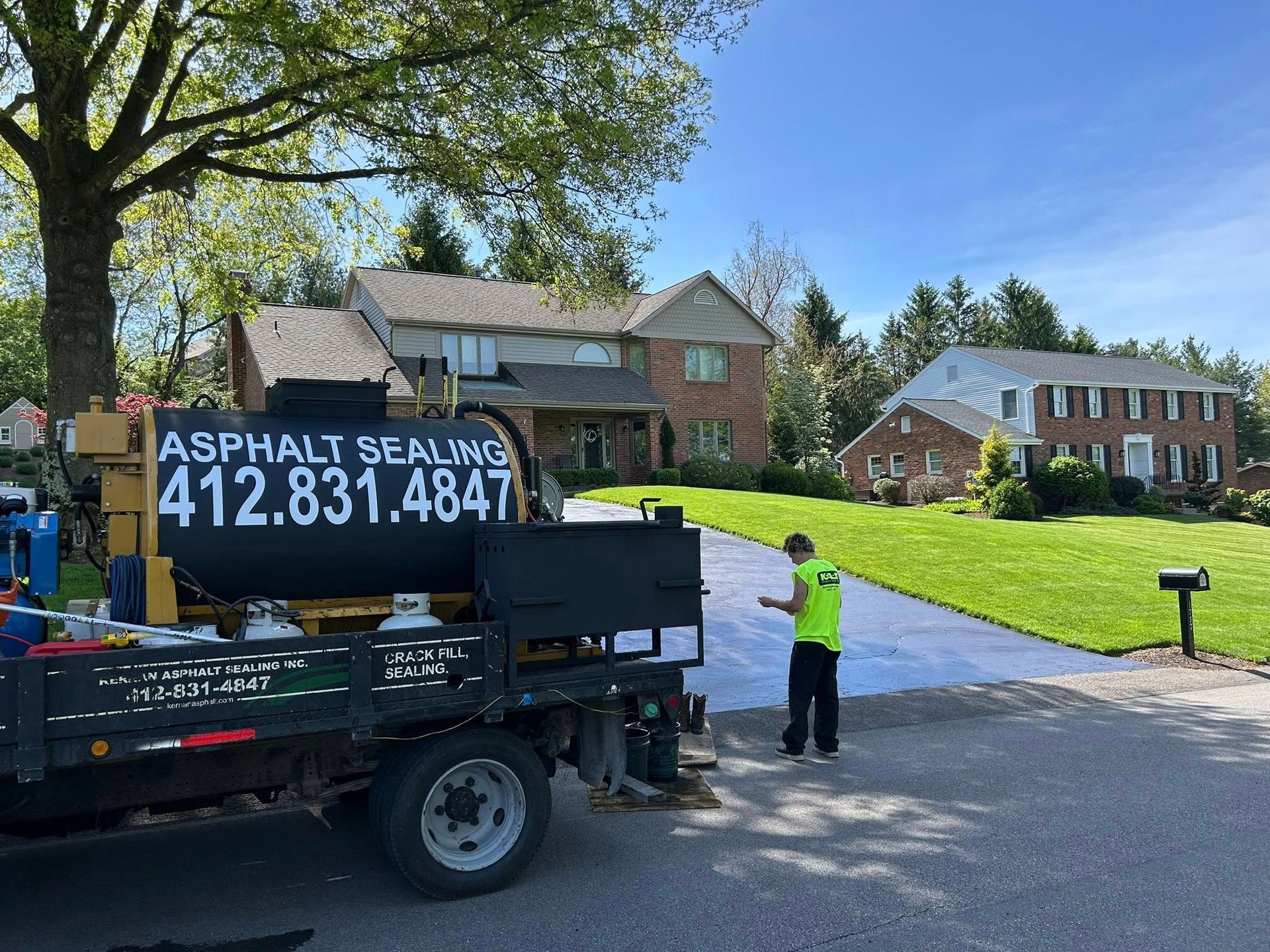 Asphalt sealing crew by a house driveway, with truck and worker in neon vest