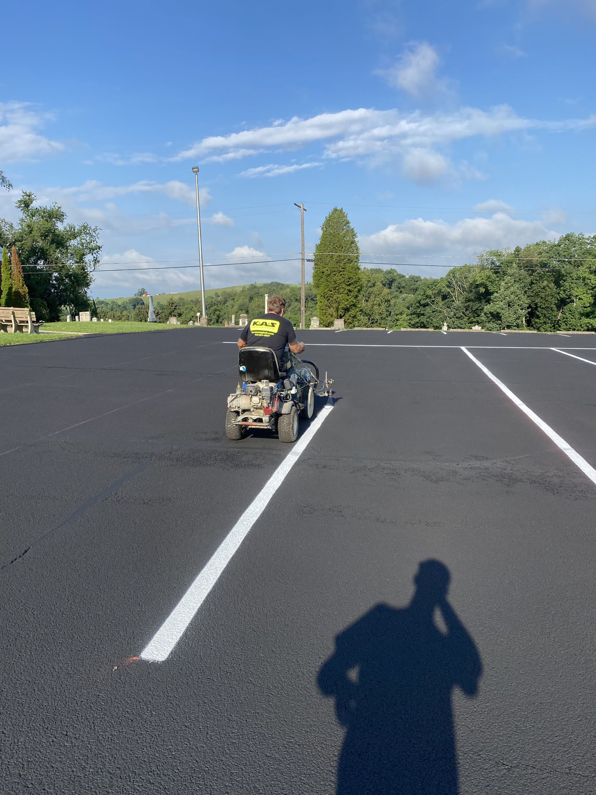 Person driving a small cart across a freshly painted black parking lot under a blue sky