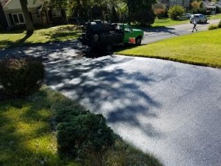 Black pickup truck with green trailer on a sunny residential driveway, lawn and houses in background