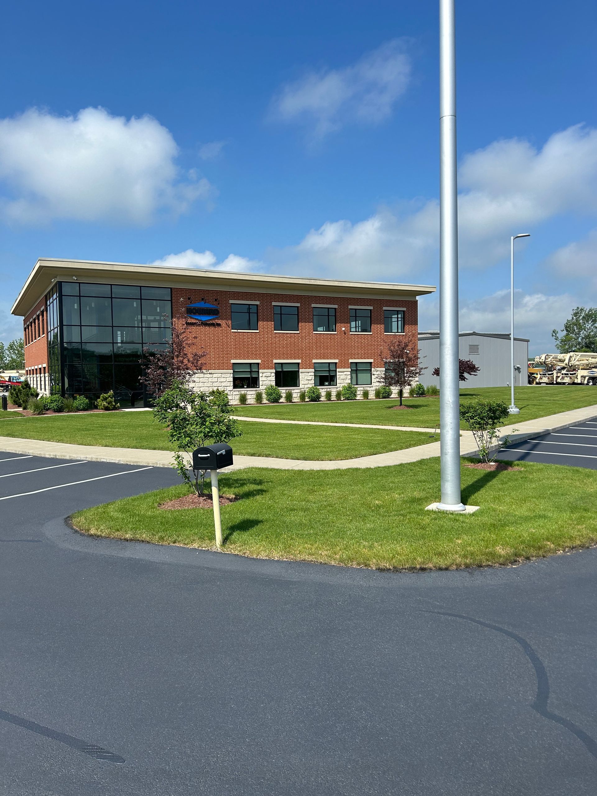 Modern brick office building with large windows, grass landscaping, and a tall flagpole under a blue sky