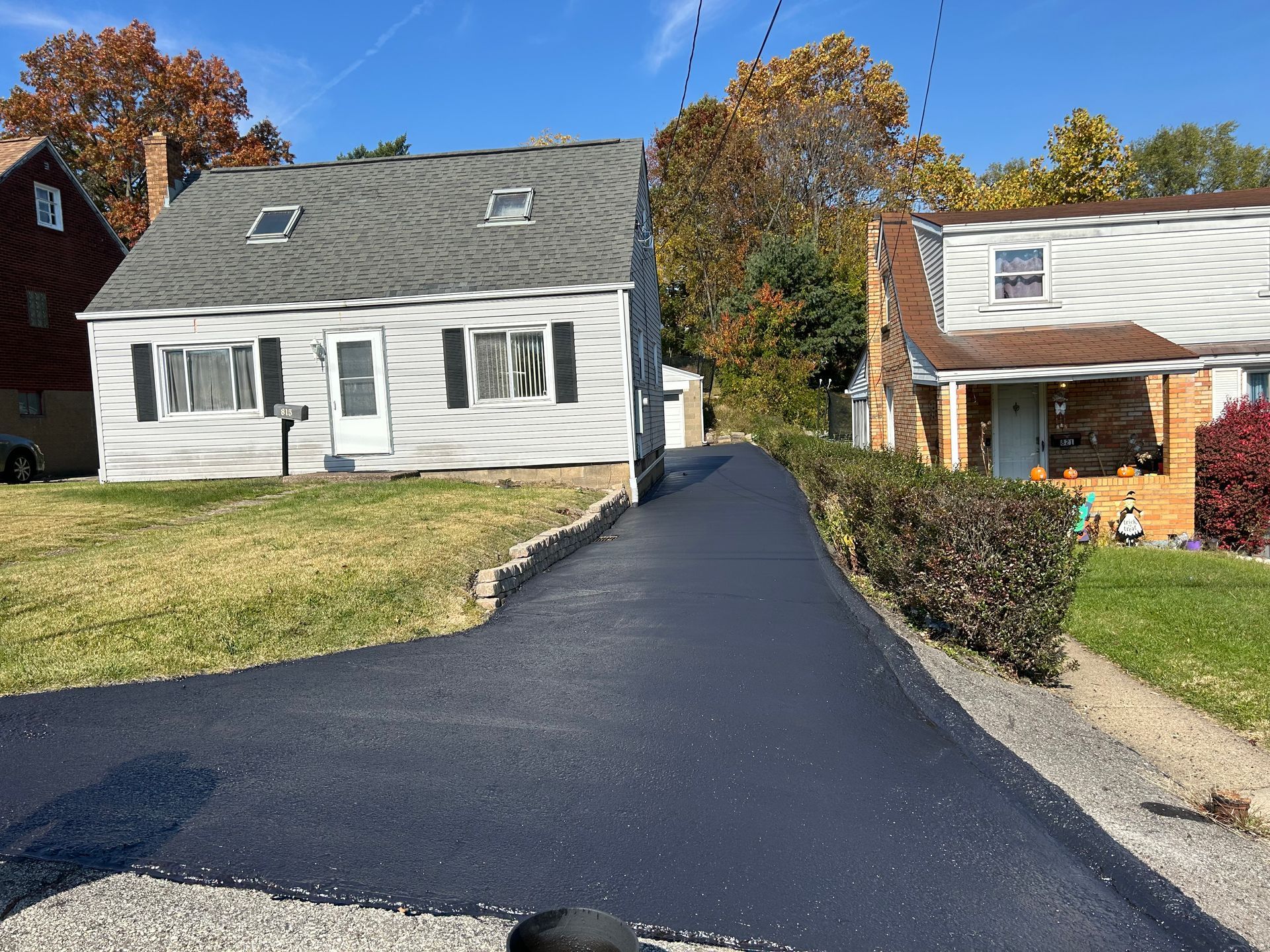 Fresh black asphalt driveway leading to a white house, with another house beside it and autumn trees behind