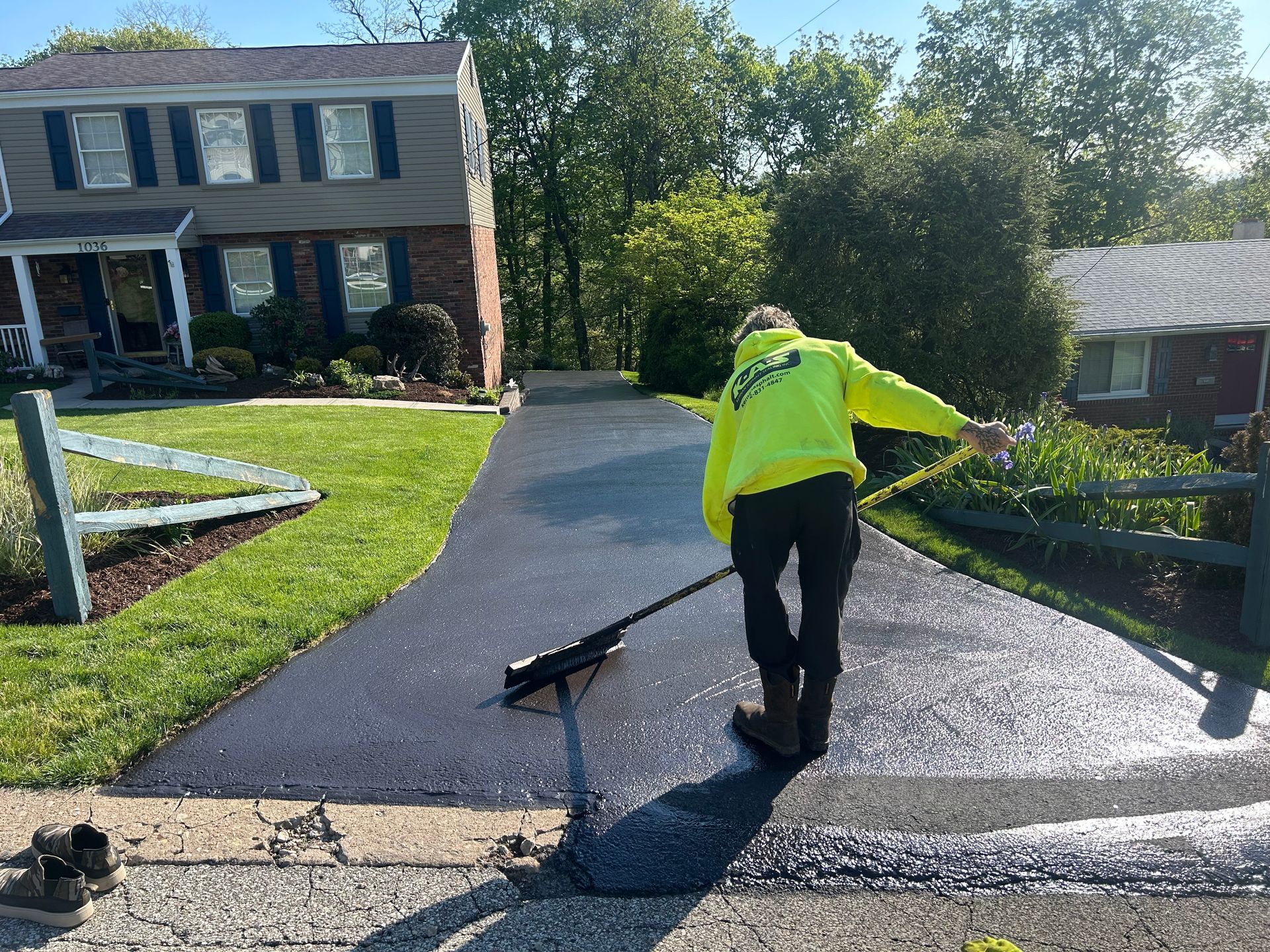 Worker in neon jacket pressure-washes a sloped driveway beside a house.
