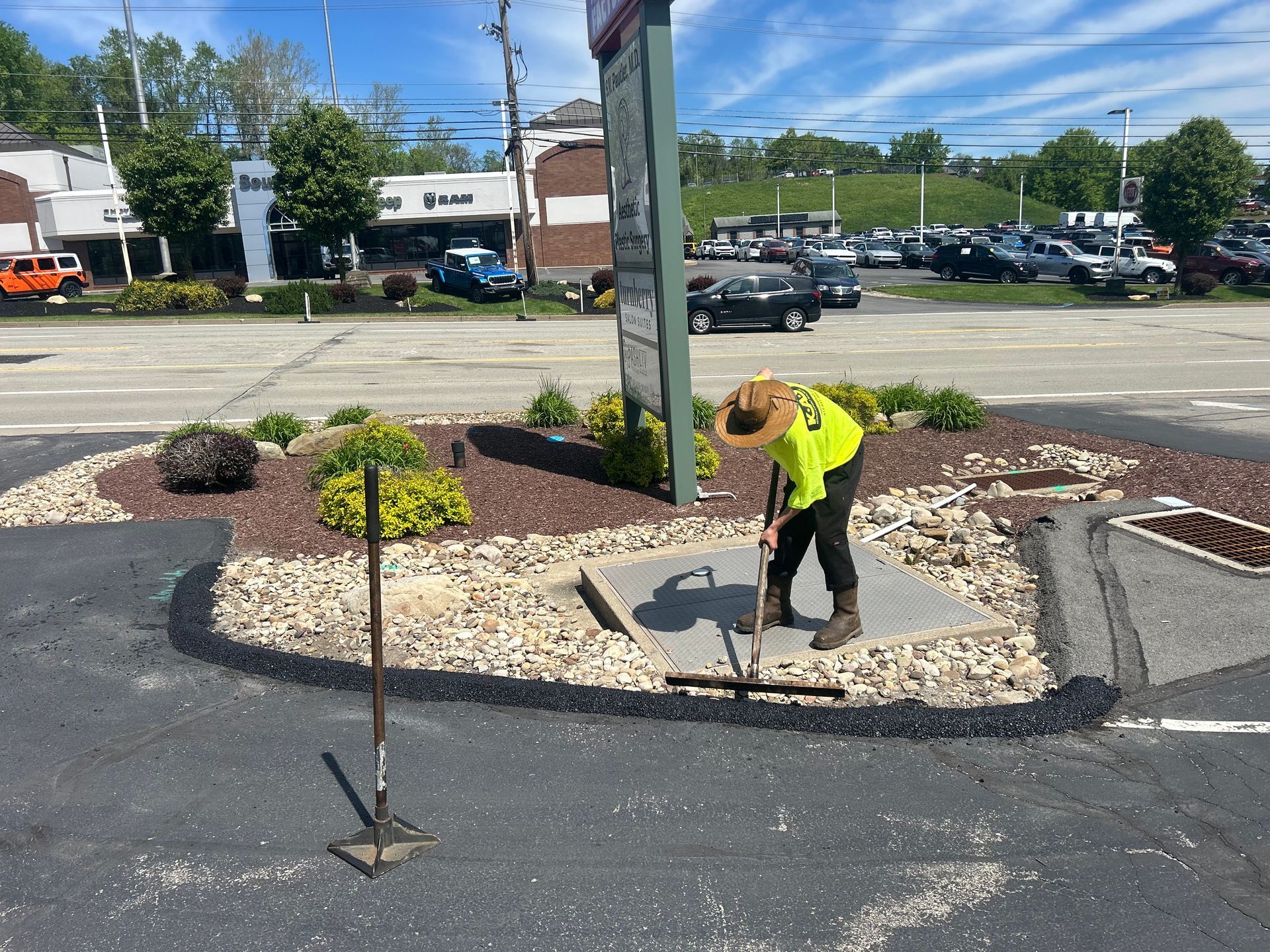 Worker in neon shirt shoveling gravel in a landscaped parking lot median.