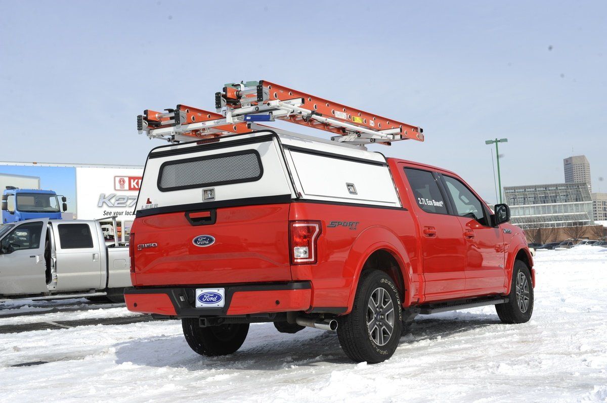 Red Ford truck with white truck cap, ladder rack, and ladders in a snowy setting.