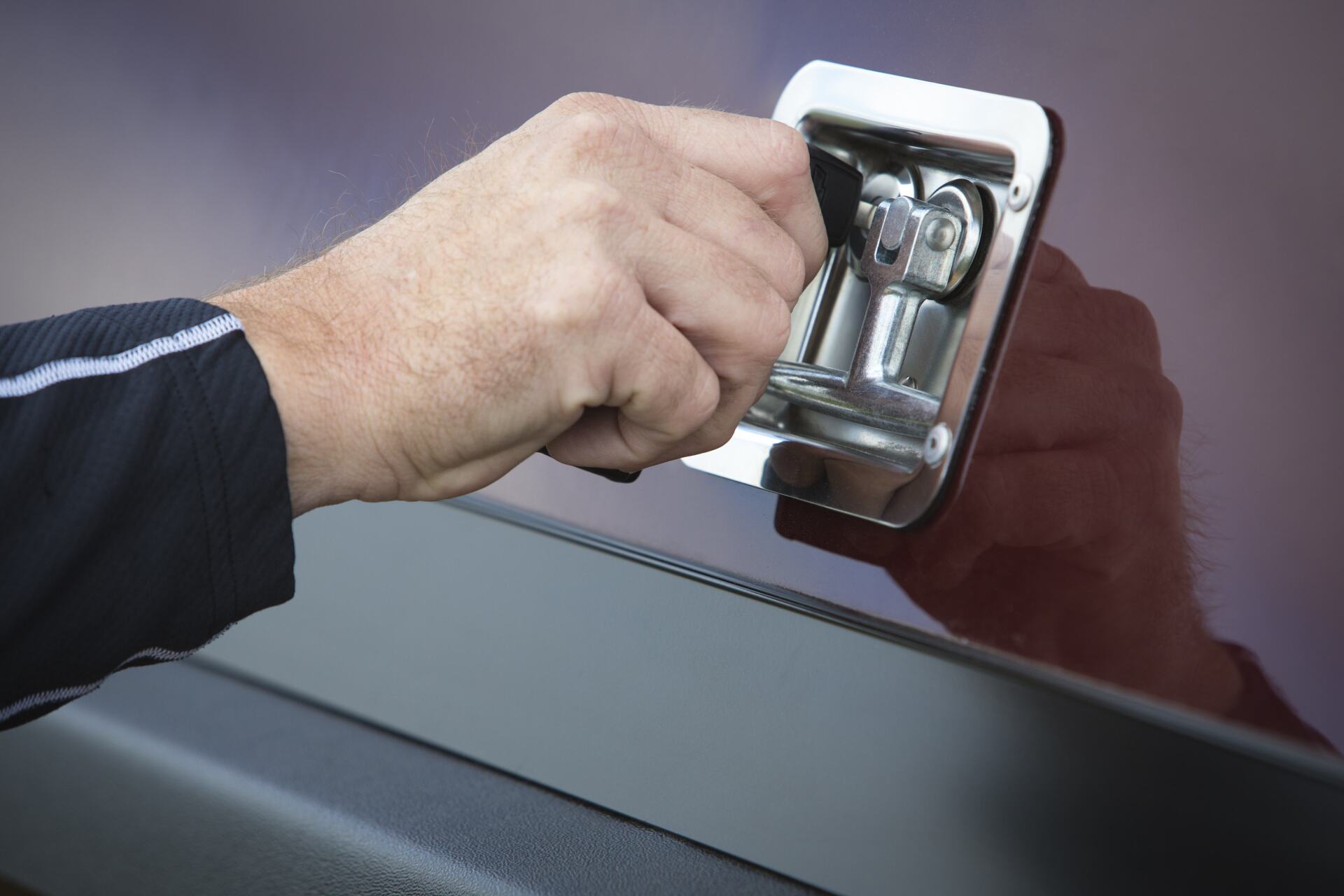 Hand turning a key in a chrome handle on a red vehicle surface.