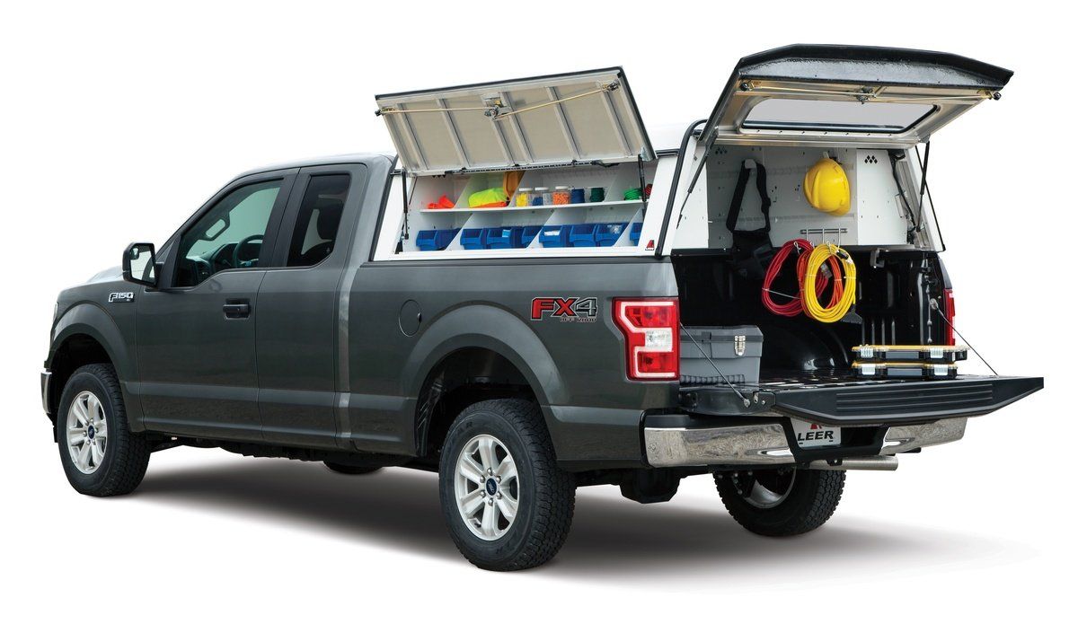 Grey pickup truck with a white utility cap; doors and tailgate open, revealing organized tools and equipment.