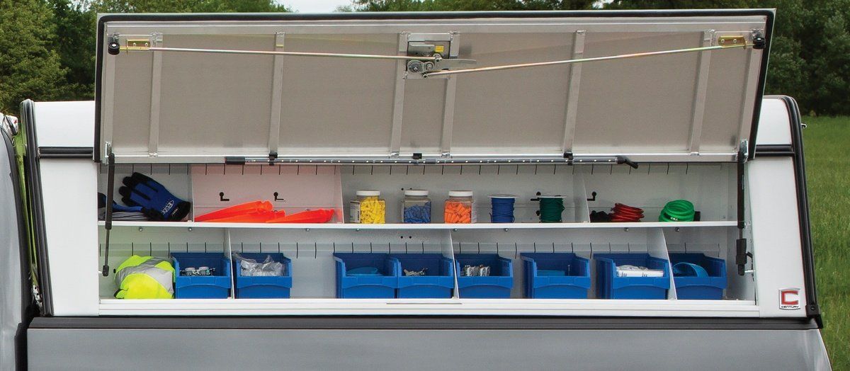 Truck bed toolbox open, revealing organized shelves with various containers and tools.
