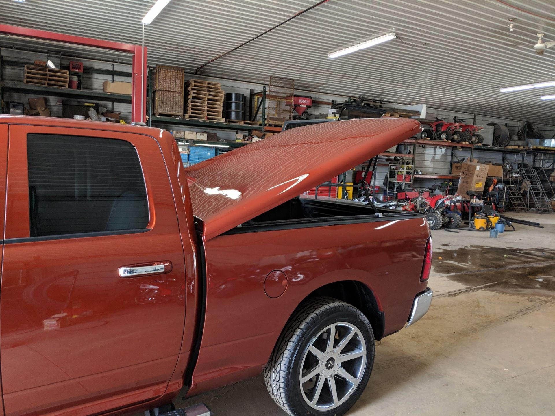 An orange pickup truck with the bed cover open in a cluttered shop setting.