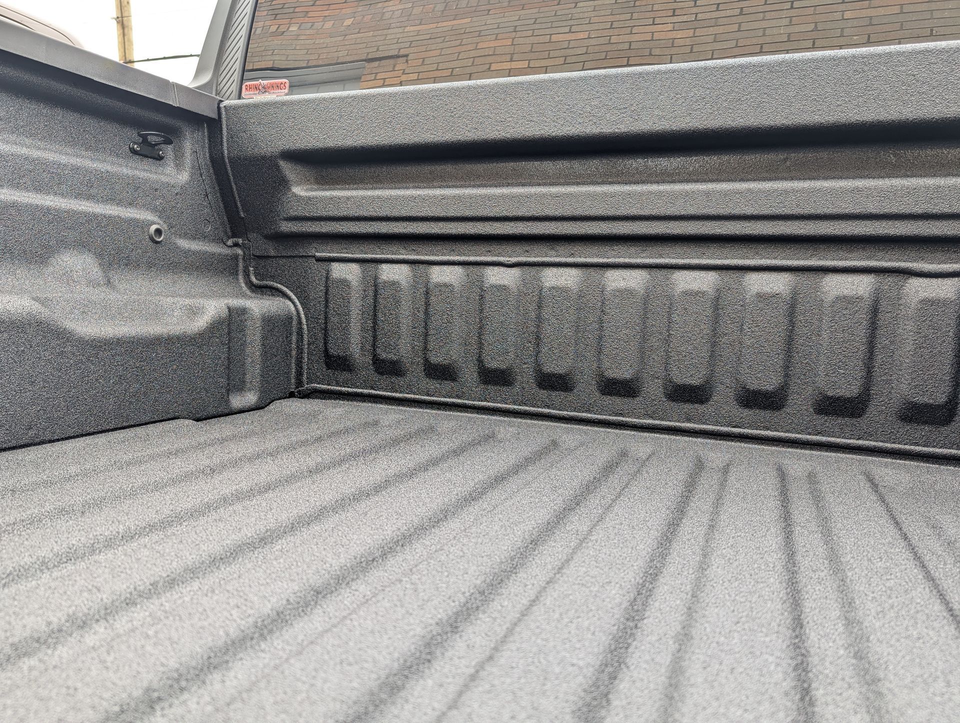 Inside a truck bed with a textured black coating, showing side wall ribs and grooves in the bed.
