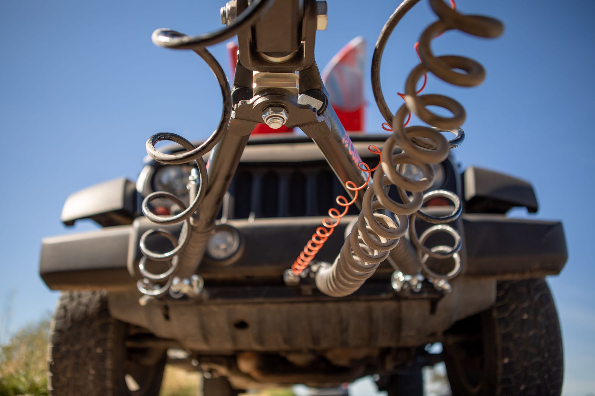 Close-up of a black Jeep's front bumper with tow-bar and coiled safety cables connected for towing.