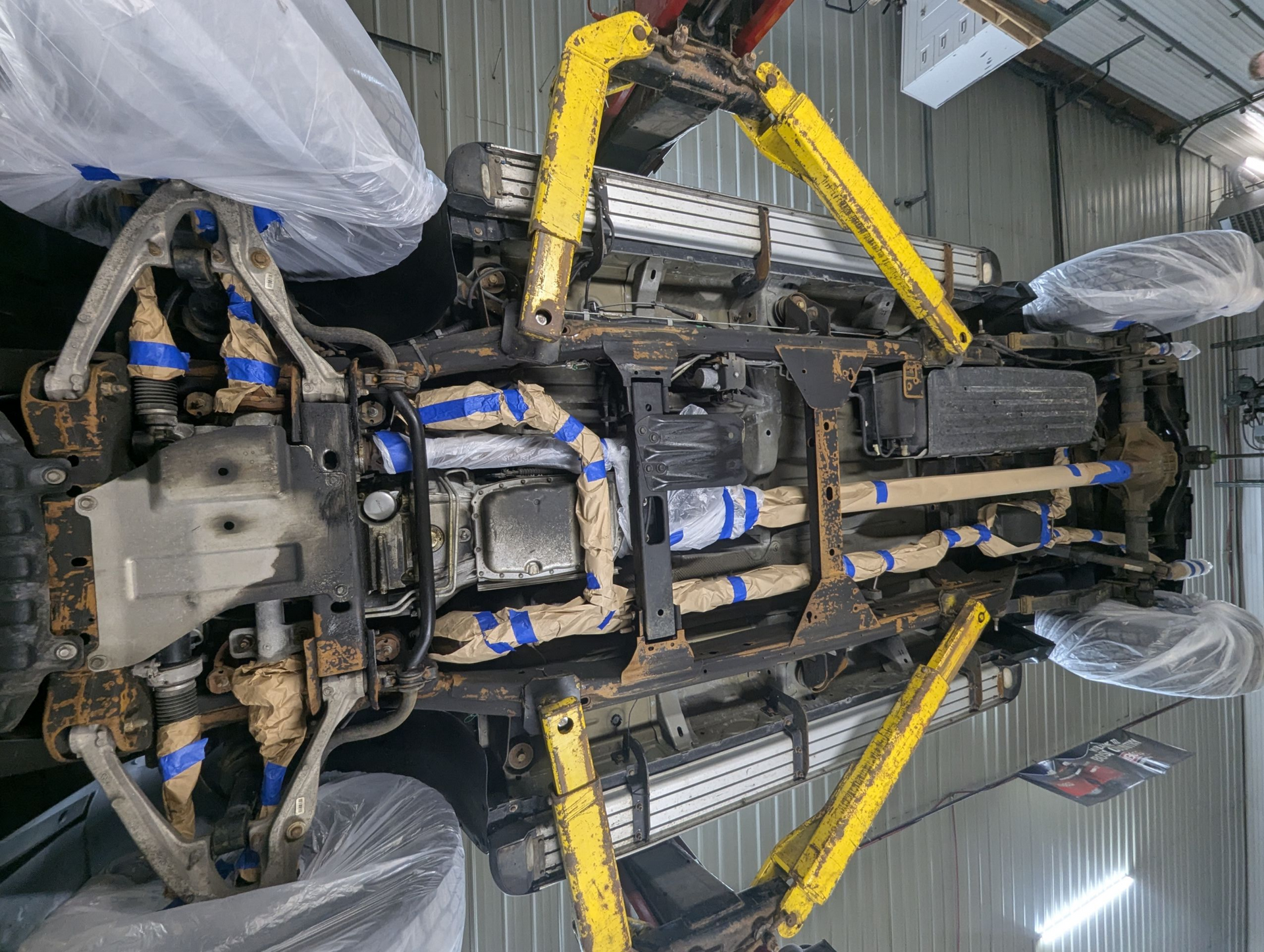 Underside of a vehicle lifted on a yellow lift in a garage; components wrapped in tape.