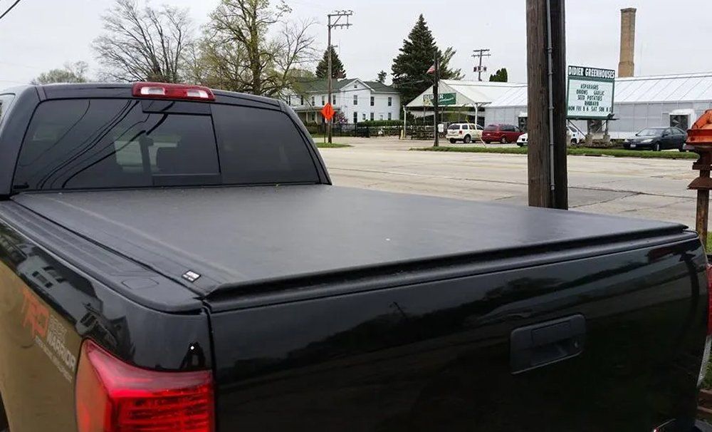 Black pickup truck with a closed Tonneau cover, parked outside a building.
