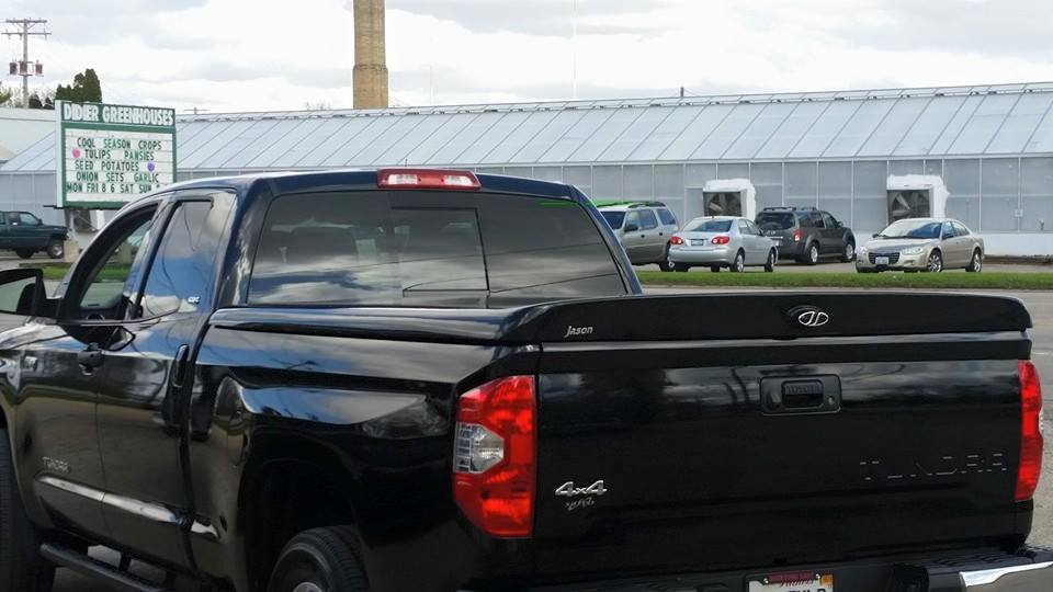 Black Toyota Tundra pickup truck in front of a greenhouse and cars, outdoor setting.