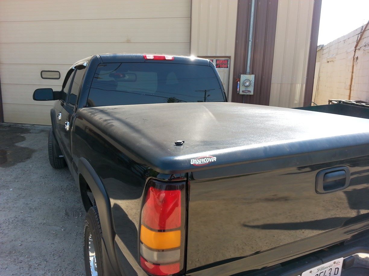 Black pickup truck with closed bed cover, parked in front of a building.
