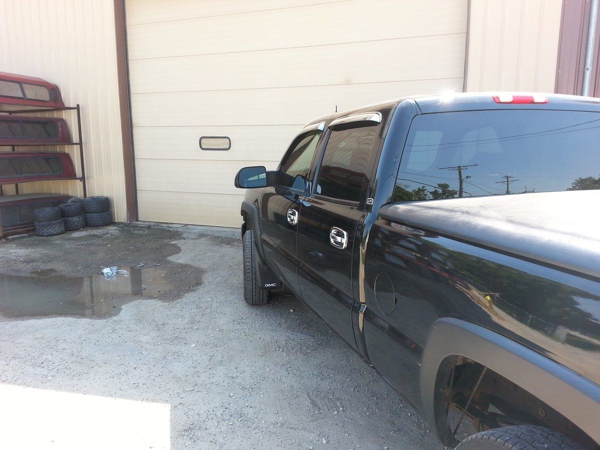 A black pickup truck was parked outside a garage. Gravel and tires in the foreground.