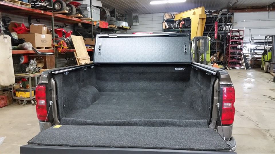 Truck bed with closed cover, lined with dark gray carpet, in a shop setting.