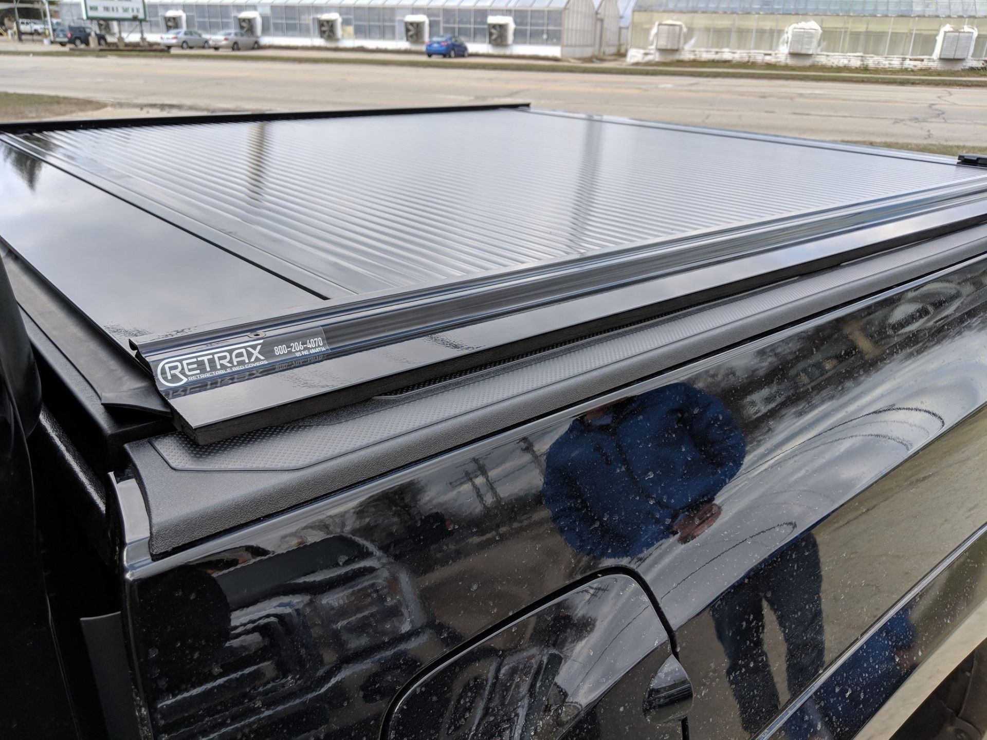 Black truck bed cover with ribbed surface; a person's reflection is visible on the truck.