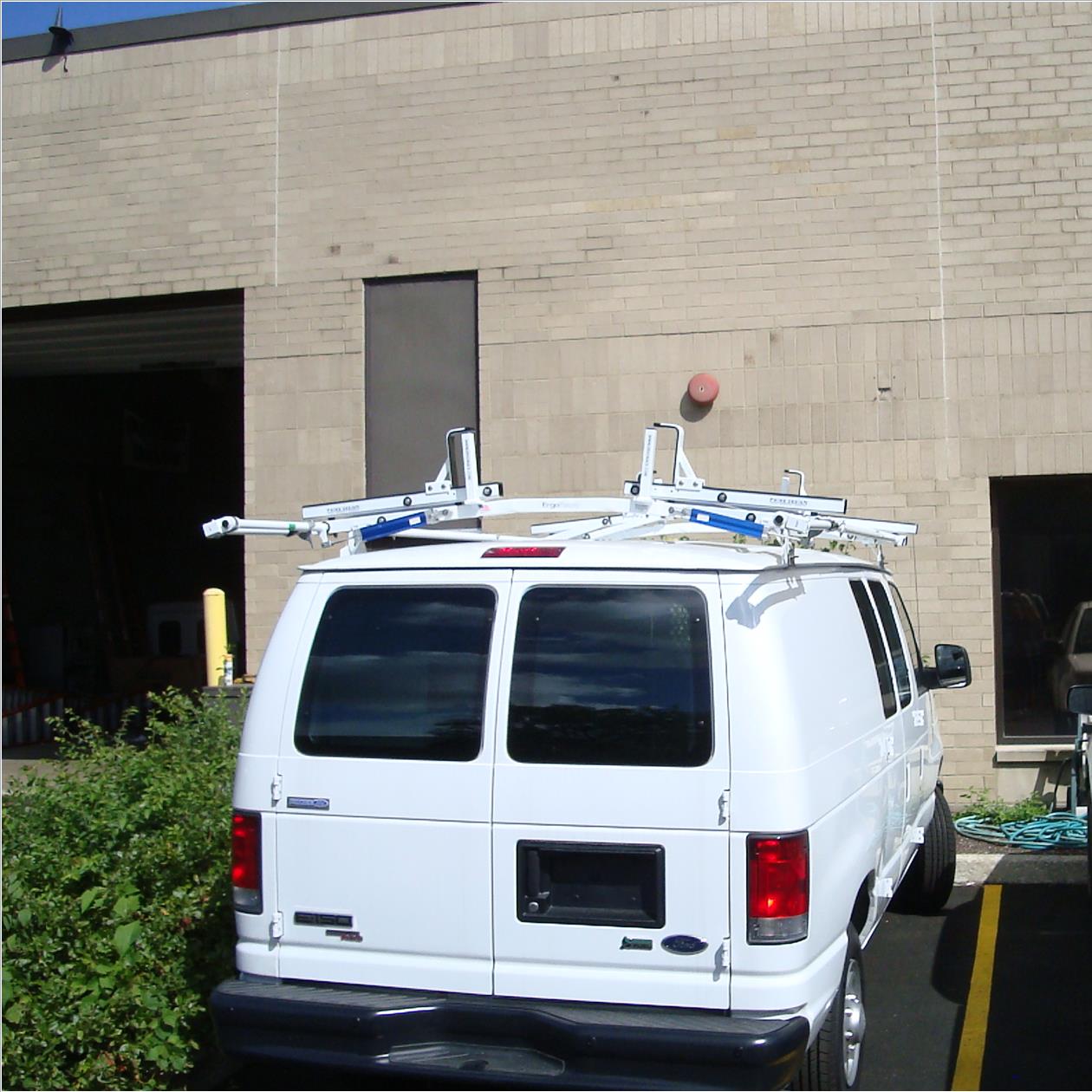 White van with a ladder rack parked in front of a brick building.
