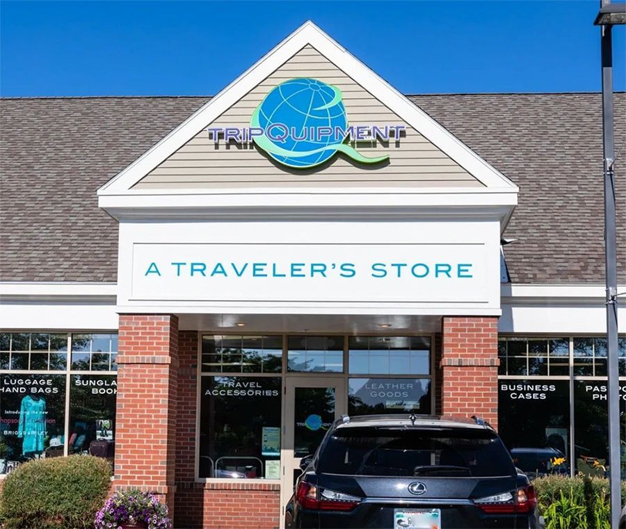 A brick storefront with a triangular sign reading "Tripment: A Traveler's Store," featuring a blue globe logo.