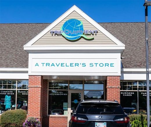 A brick storefront with a triangular sign reading "Tripment: A Traveler's Store," featuring a blue globe logo.