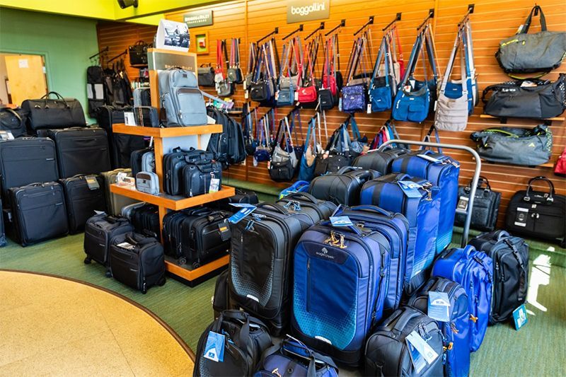 A luggage store display filled with various travel bags, including suitcases on the floor and handbags on wall racks.