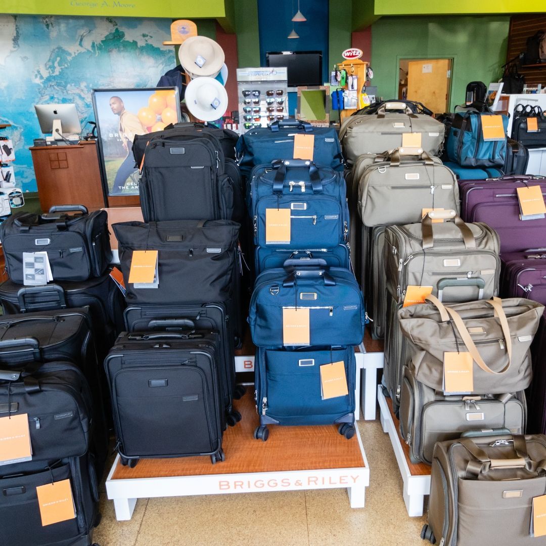 A retail display of Briggs & Riley rolling suitcases and travel bags in black, blue, and tan on a store floor.
