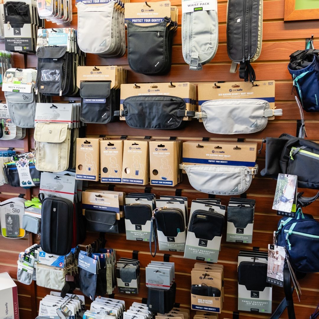 A store display wall filled with various travel bags and accessories in neutral colors like black, gray, and beige.