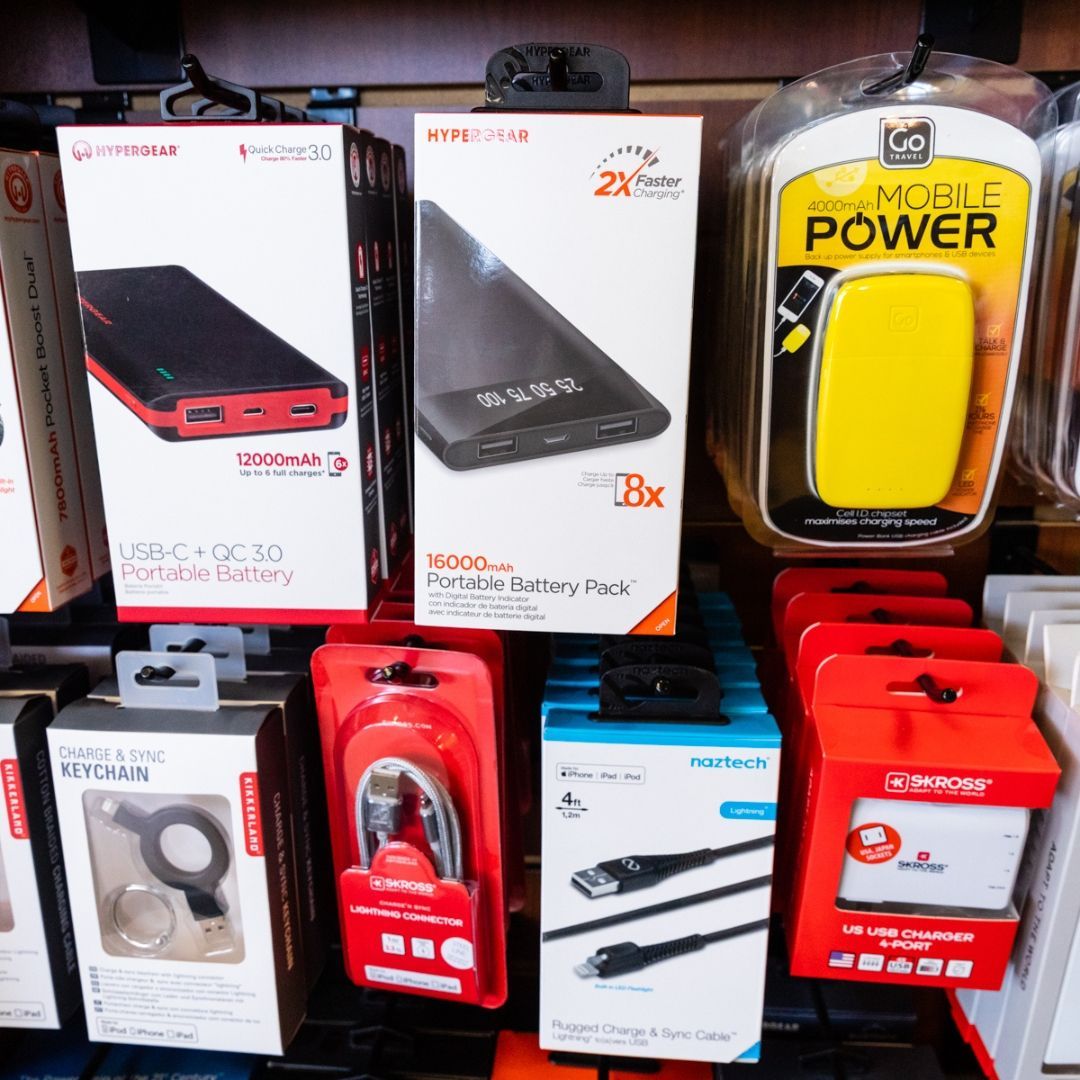 A retail store shelf displays various portable battery packs, charging cables, and power adapters in their original boxes.