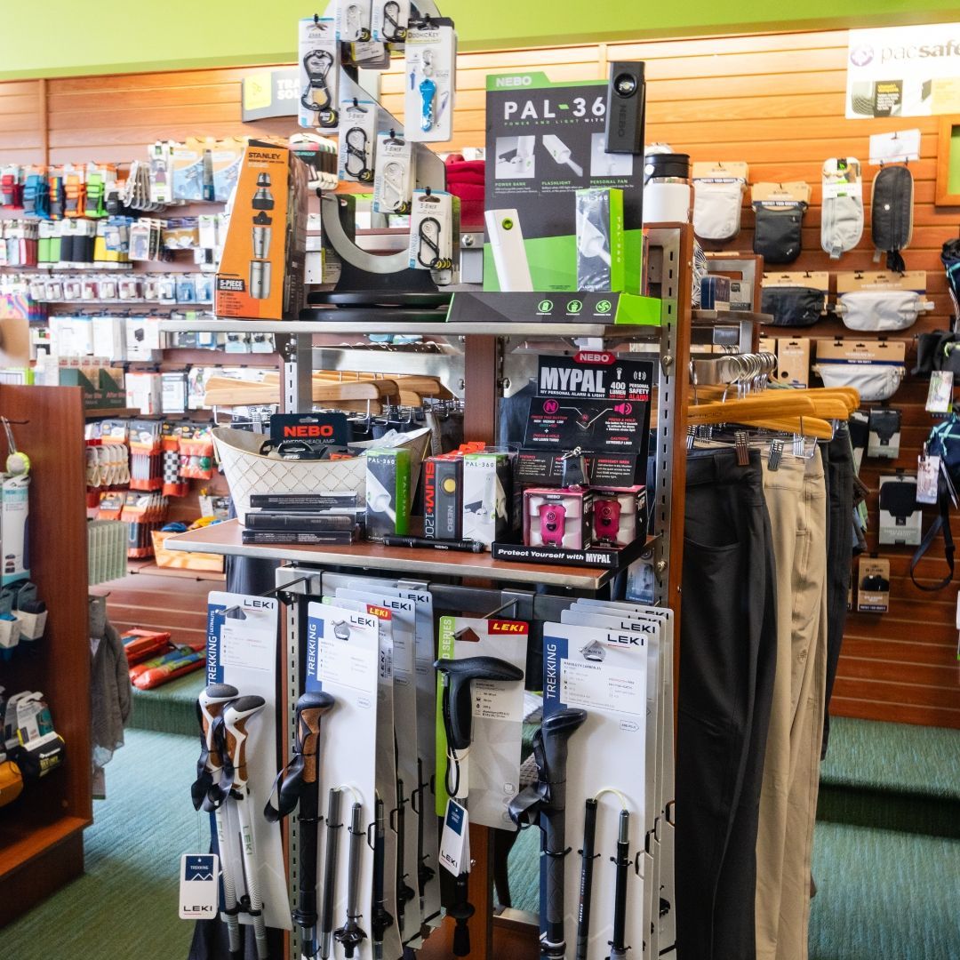 A retail store display featuring hiking poles, small electronics, and various outdoor gear items on wooden shelves.