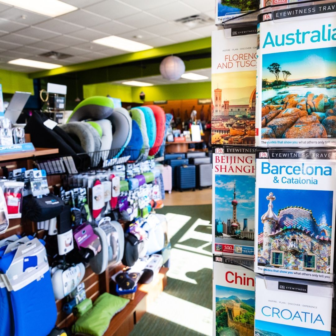 A travel shop display featuring colorful neck pillows on the left and a rack of destination guidebooks on the right.