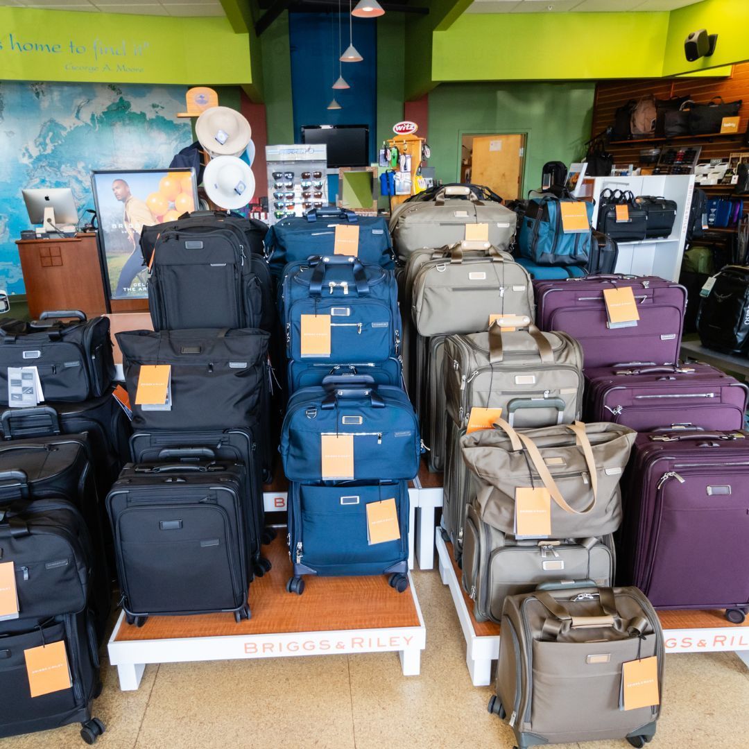 A luggage store display featuring black, blue, purple, and gray rolling suitcases stacked on wooden platforms.