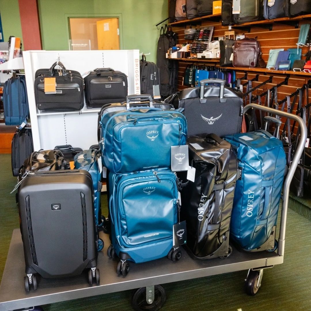 A luggage cart in a store displaying various suitcases and duffel bags, including several blue Osprey brand items.