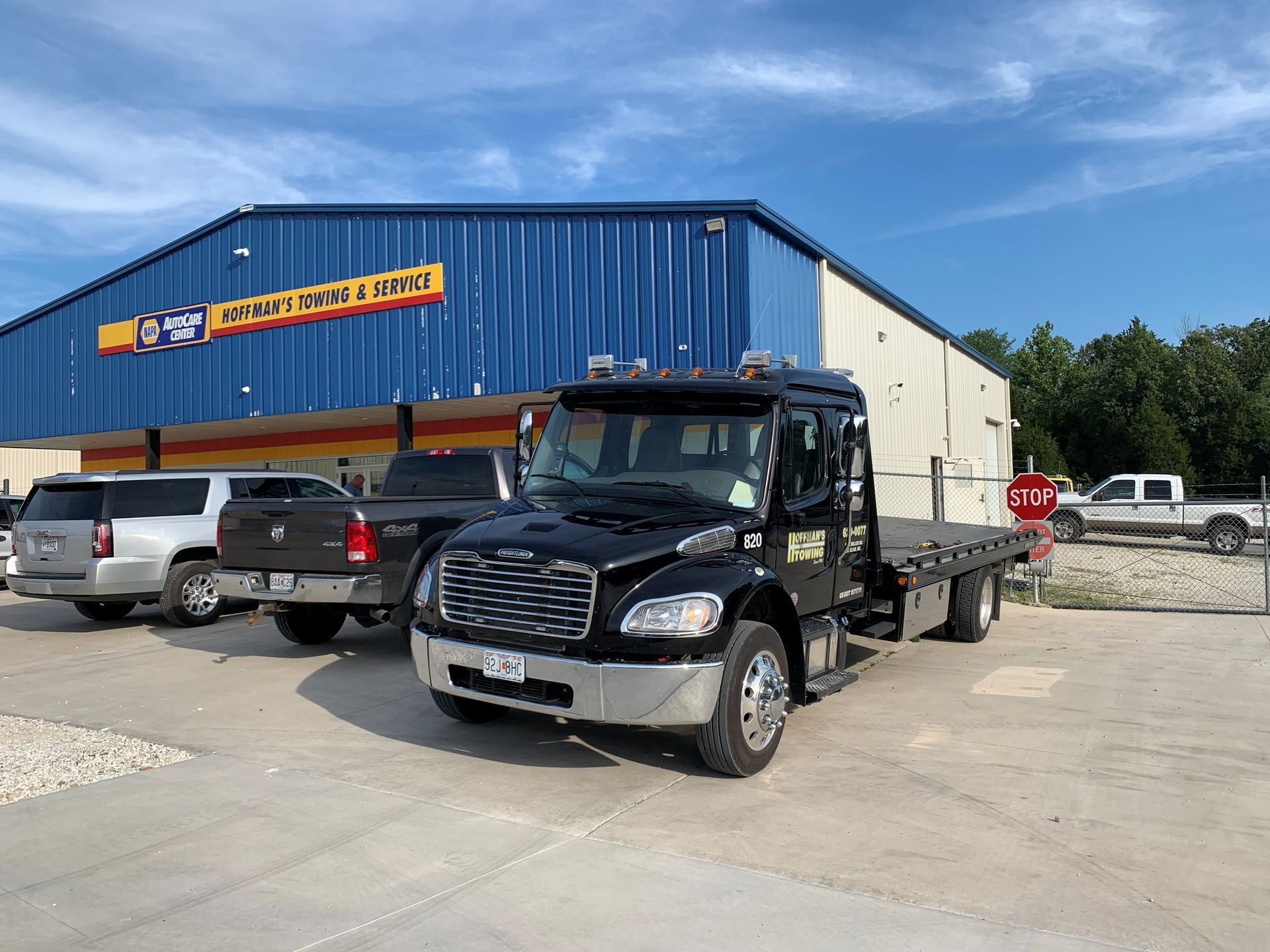 Black tow truck parked in front of a blue building with vehicles.