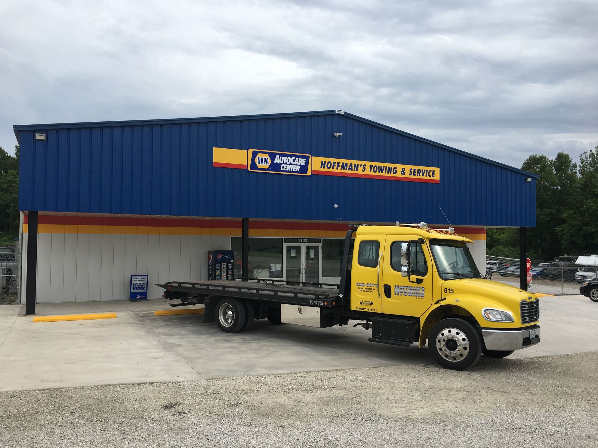 Yellow tow truck parked outside a blue and yellow auto parts store.