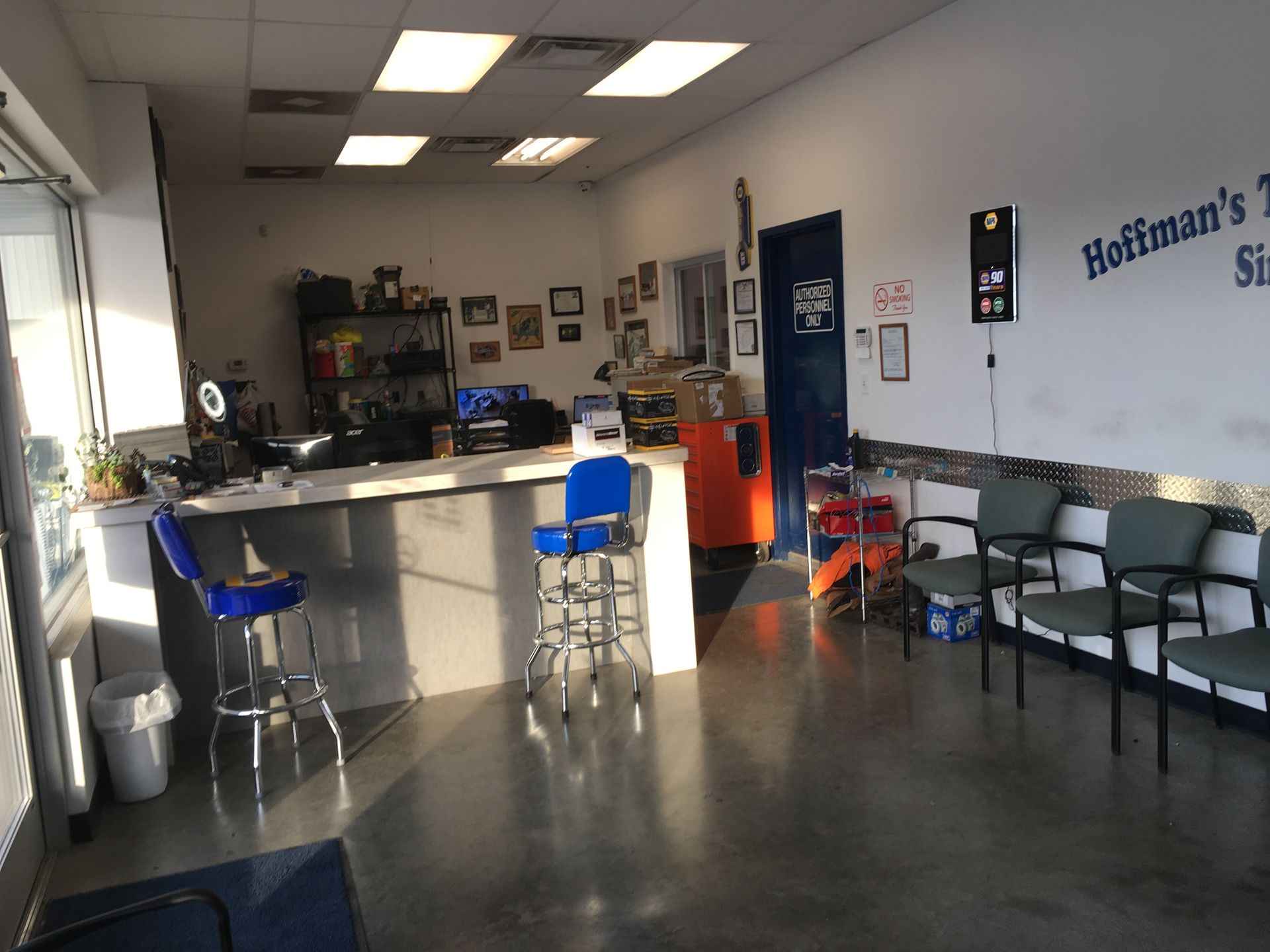 Interior of a waiting area in an auto shop. A counter, chairs, and door are visible. Bright light enters the space.