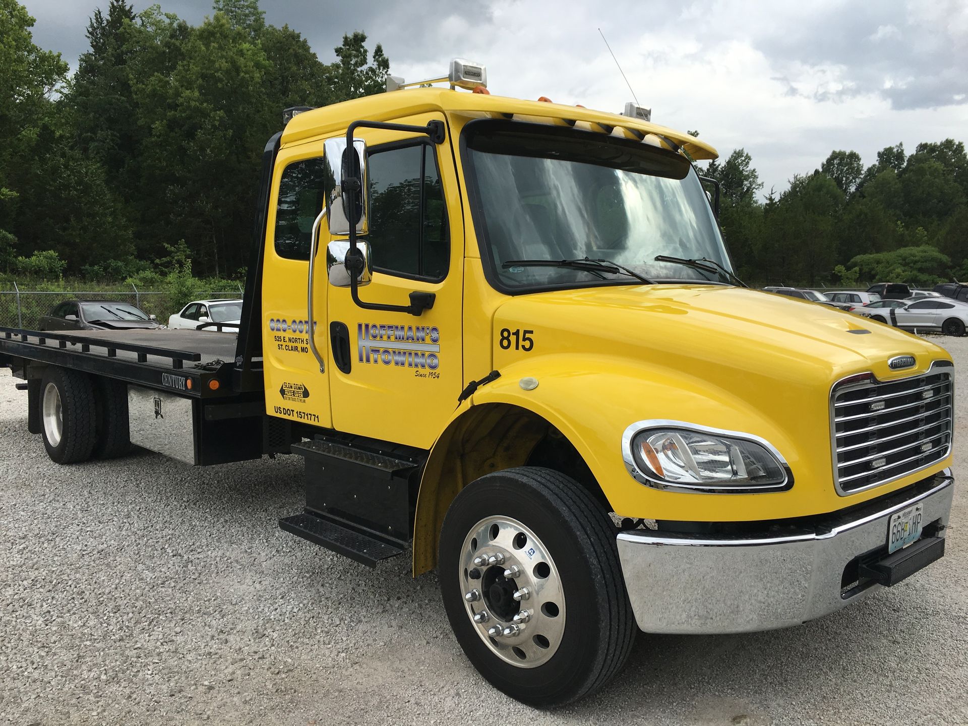 Yellow tow truck parked outdoors on gravel, with a flatbed.