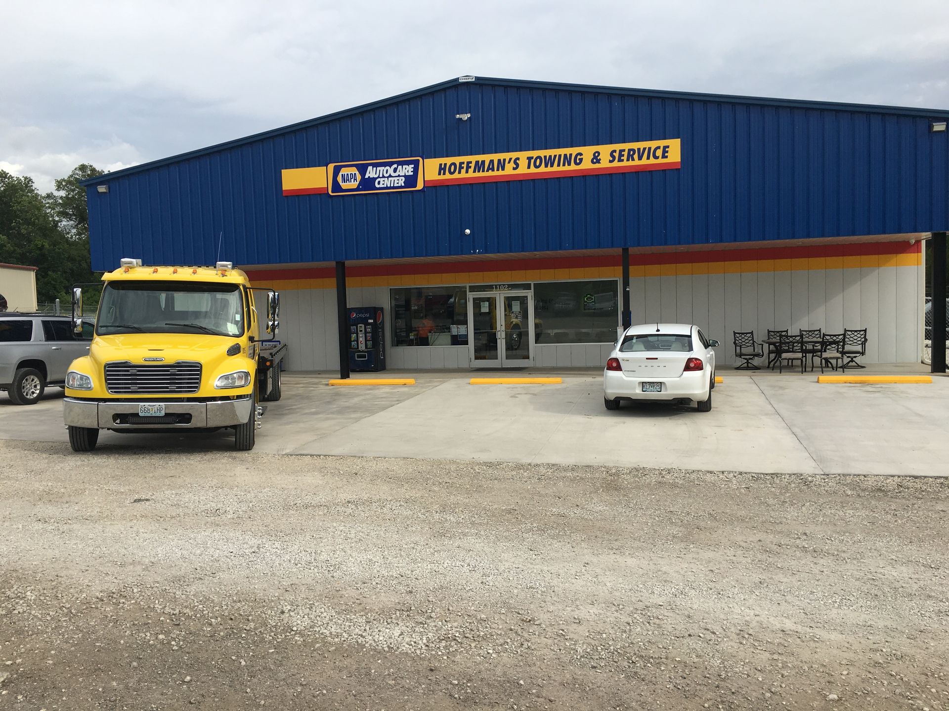 A yellow tow truck parked in front of an auto parts store with blue and tan facade.