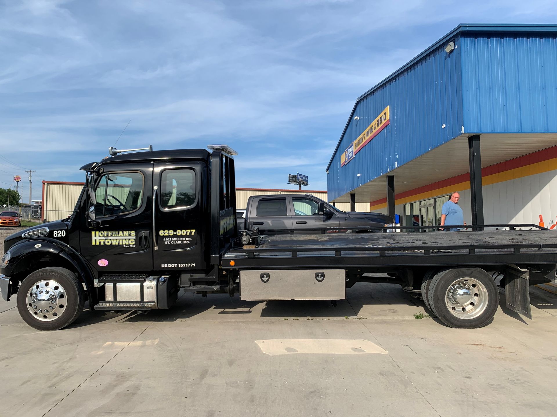 Tow truck with a gray pickup truck on its flatbed, parked in front of a blue building.