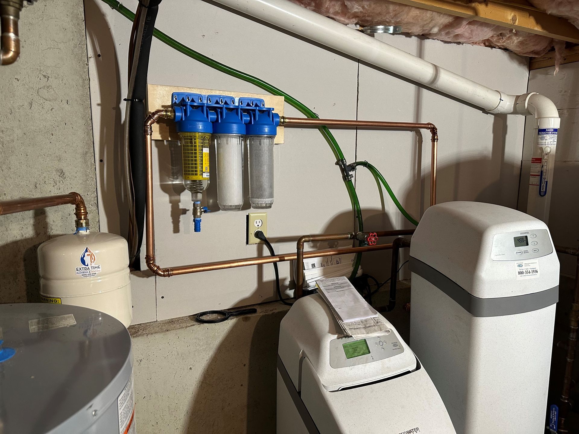 A water softener is sitting in a basement next to a water heater.