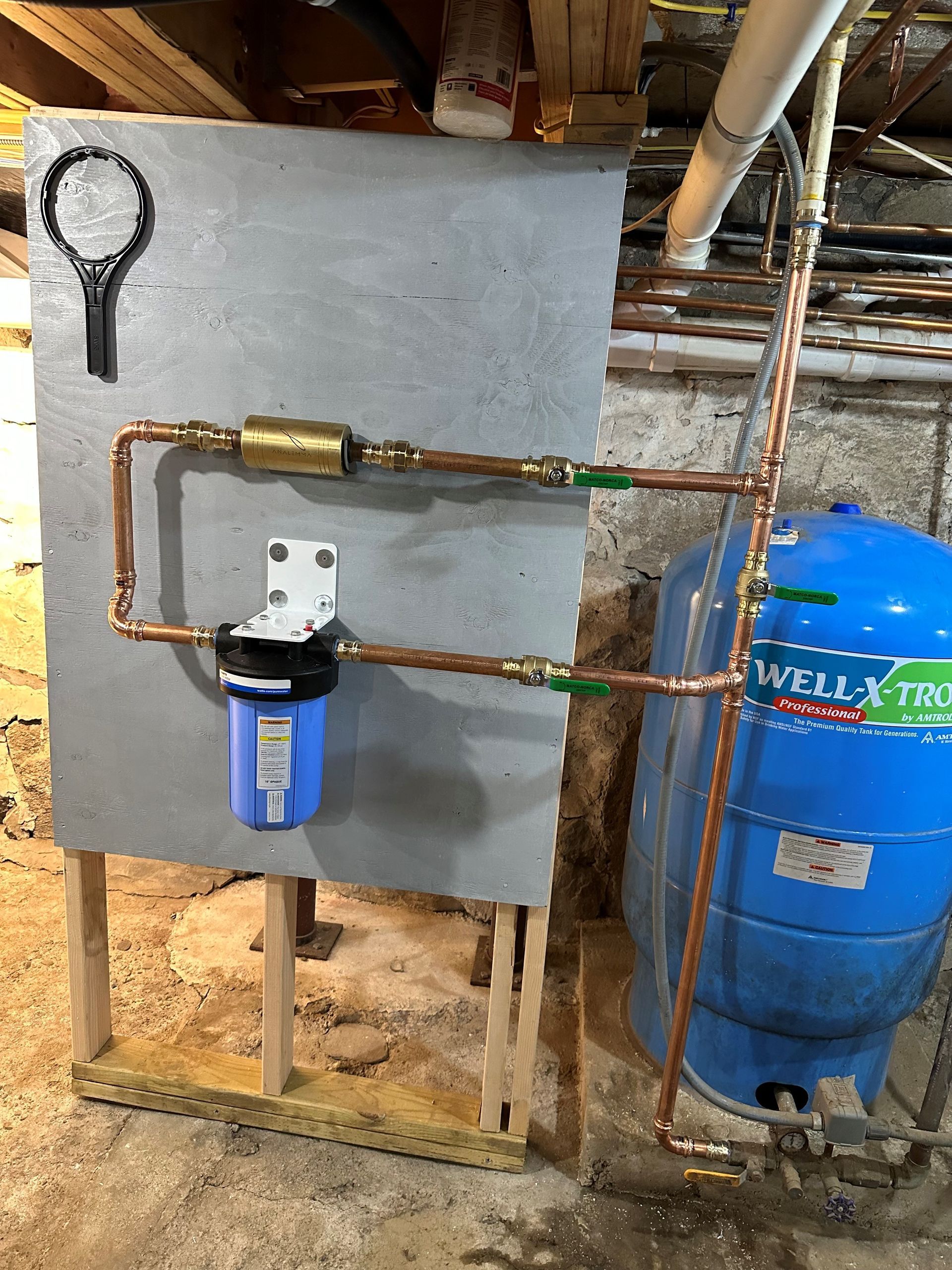 A blue water tank is sitting next to a copper pipe.