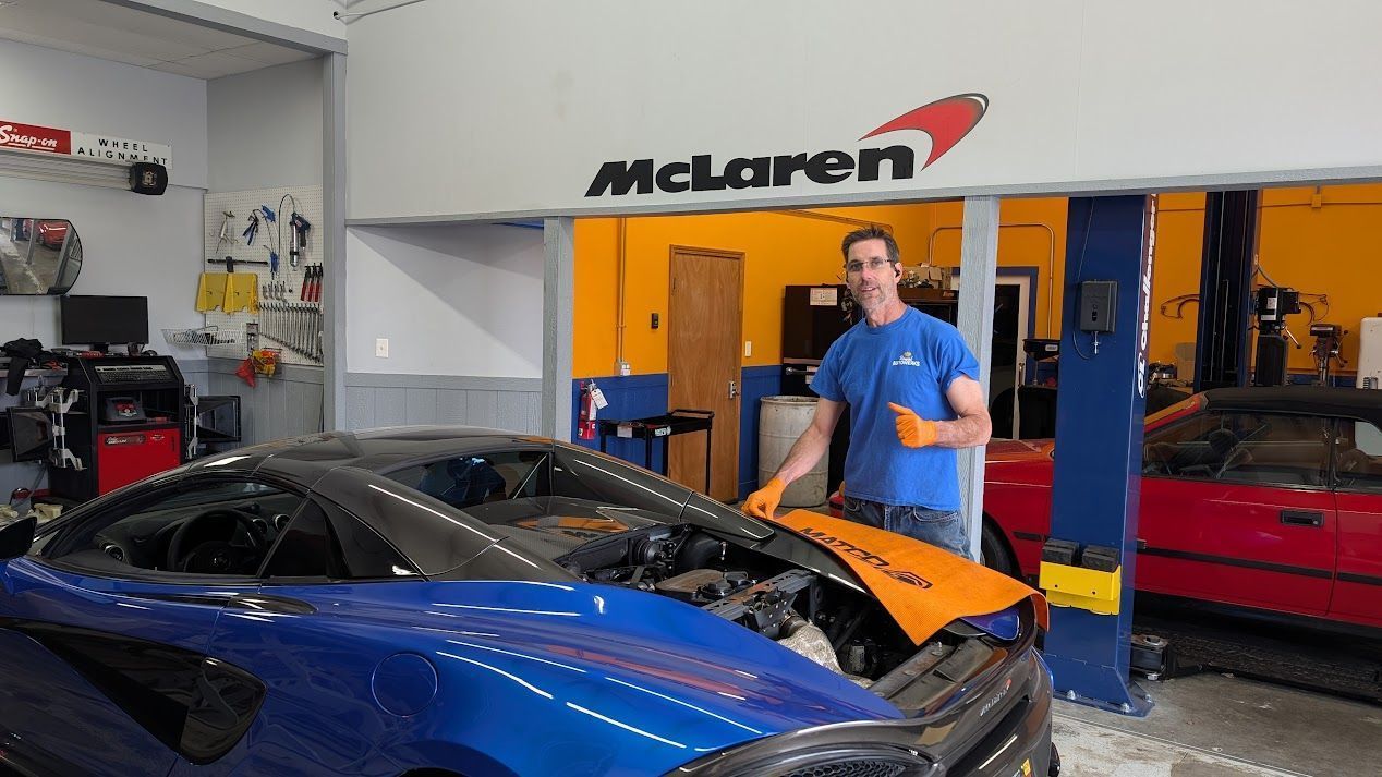 Man in blue shirt beside blue and orange sports cars in a McLaren garage