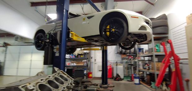 A white car on a lift in a garage with a disassembled engine in the foreground.