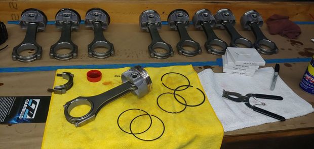 Engine pistons, rods, rings, and tools on a workbench.