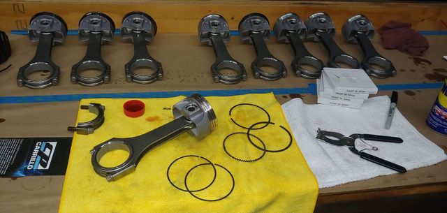 Engine pistons, rods, rings, and tools on a workbench.