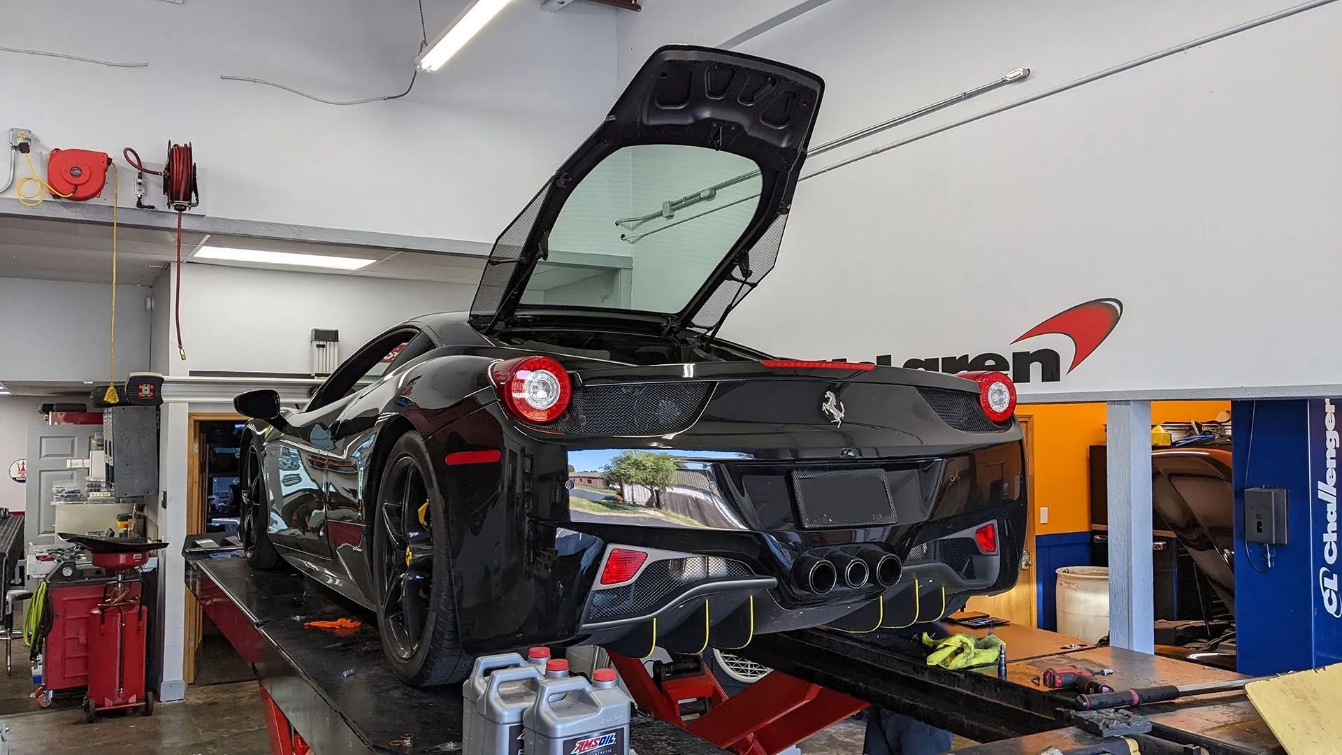 Black Ferrari on a lift in a garage with its hatch open, ready for service.