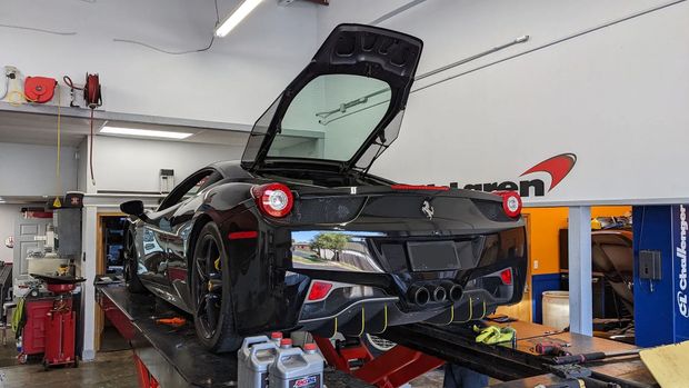 Black Ferrari sports car on a lift inside a garage, rear hatch open.